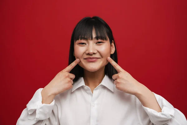 年轻的亚洲女人微笑着 用手指指指着被红色背景隔开的脸颊 — 图库照片