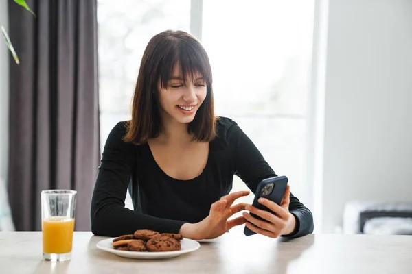Щаслива Молода Біла Жінка Дивиться Мобільний Телефон Сидячи Кухонним Столом — стокове фото