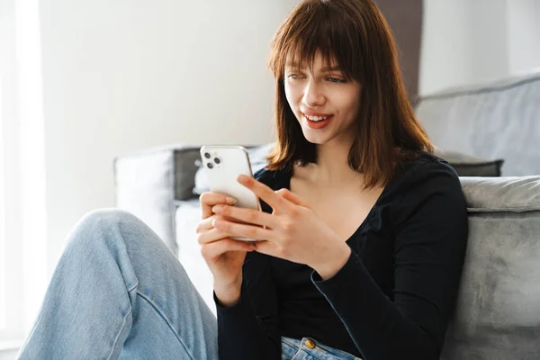 Усміхнена Молода Жінка Тримає Мобільний Телефон Сидячи Дивані Вдома — стокове фото