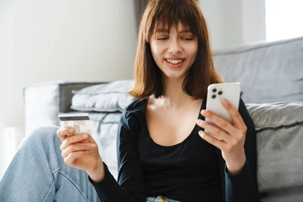 Mosolygó Fiatal Online Vásárlás Mobiltelefon Tartja Hitelkártya Miközben Kanapén Otthon — Stock Fotó