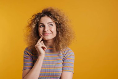 Sarı duvarın arkasında dikilmiş, köpüklü saçları olan, dalgın, genç, sarışın bir kadın.