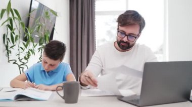 Babası ev ödevlerini yaparken dizüstü bilgisayarını kullanıyor.