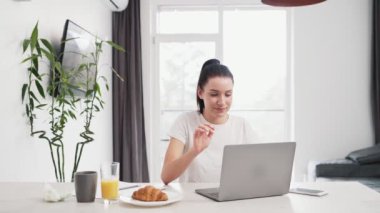 Evde video bağlantısı ile konuşurken bilgisayarını kullanan gülümseyen bir kadın.