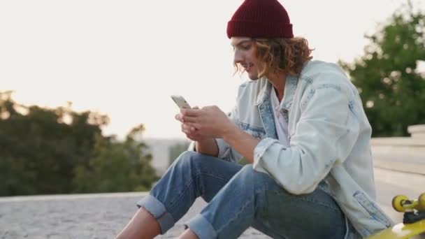 Szczęśliwy Deskorolkarz Dżinsach Korzystający Telefonu Siedzący Schodach Zewnątrz — Wideo stockowe