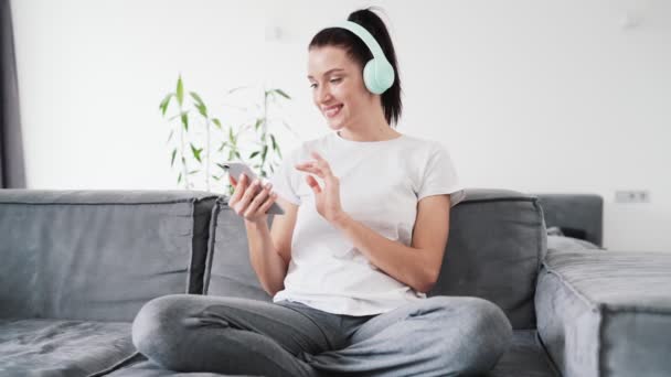 Una Mujer Feliz Usando Auriculares Mientras Escucha Música Sentada Sofá — Vídeo de stock