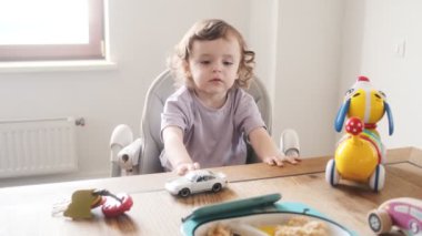 Güzel bir bebek çocuk koltuğunda oturuyor ve evdeki mutfakta cep telefonunu izliyor.