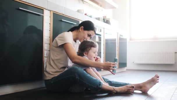 幸せな母親は自分の子供と一緒に台所の床に座って写真を撮る — ストック動画