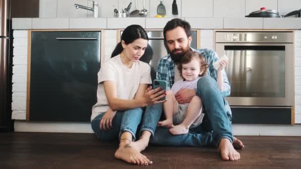 床に座っている携帯電話で何かを一緒に見て楽しい家族の時間を過ごす — ストック動画