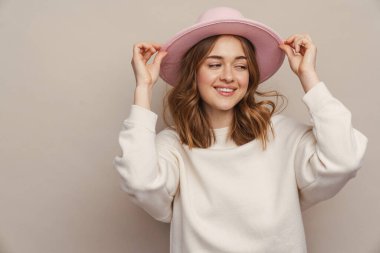 Şapkalı, gülümseyen ve gri arka planda mahsur kalmış genç bir kadın.