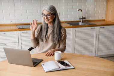 Mutfakta dizüstü bilgisayarla çalışırken kulaklık takan gülümseyen kadın.
