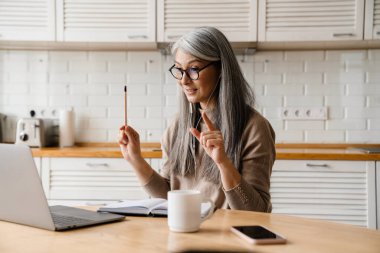 Mutfakta dizüstü bilgisayarla çalışırken kulaklık takan gülümseyen kadın.