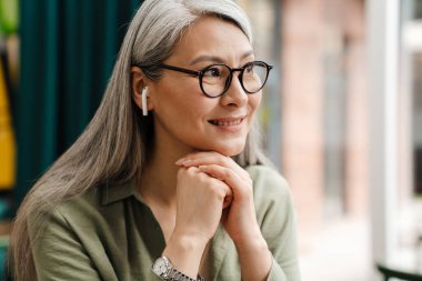 Evde kulaklıkla müzik dinlerken gülümseyen olgun gri kadın.