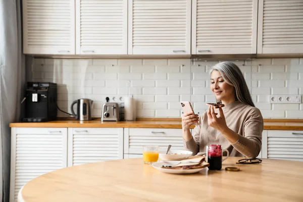 미소짓는 집에서 식사를 하면서 핸드폰을 사용하는 — 스톡 사진