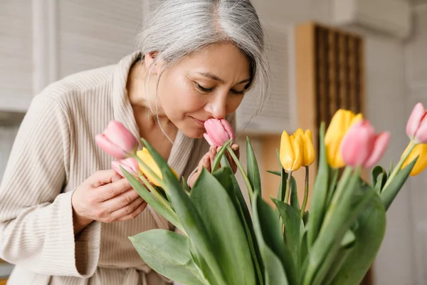 Starší Šedá Žena Županu Vonící Tulipány Kuchyni Doma — Stock fotografie