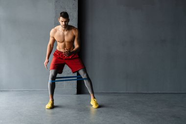 Genişletici bantla egzersiz yapan genç üstsüz sporcu.