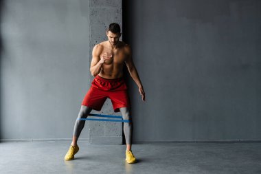 Genişletici bantla egzersiz yapan genç üstsüz sporcu.