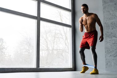 Genişletici bantla egzersiz yapan genç üstsüz sporcu.