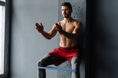 Genişletici bantla egzersiz yapan genç üstsüz sporcu.