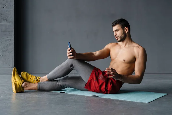 年轻的赤身裸体运动员在室内锻炼的时候用手机自拍 — 图库照片