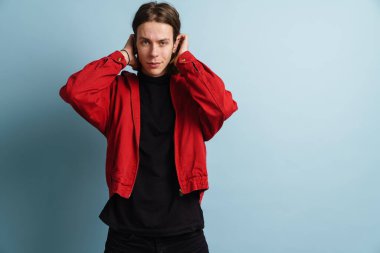 Mavi arka planda duran ceketli genç sarışın bir adamın portresi.