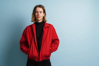 Mavi arka planda duran ceketli genç sarışın bir adamın portresi.