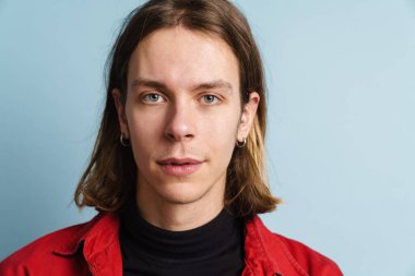 Kırmızı ceketli genç beyaz adam mavi duvarın üzerinden izole edilmiş kameraya bakıyor.