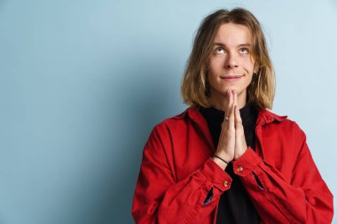 Avuç içlerini bir arada tutarken gülümseyen genç beyaz adam mavi duvarın üzerinde izole edilmiş.