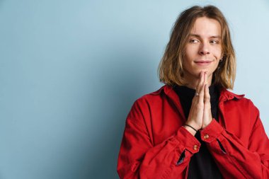 Avuç içlerini bir arada tutarken gülümseyen genç beyaz adam mavi duvarın üzerinde izole edilmiş.