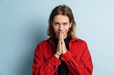 Avuç içlerini bir arada tutarken gülümseyen genç beyaz adam mavi duvarın üzerinde izole edilmiş.