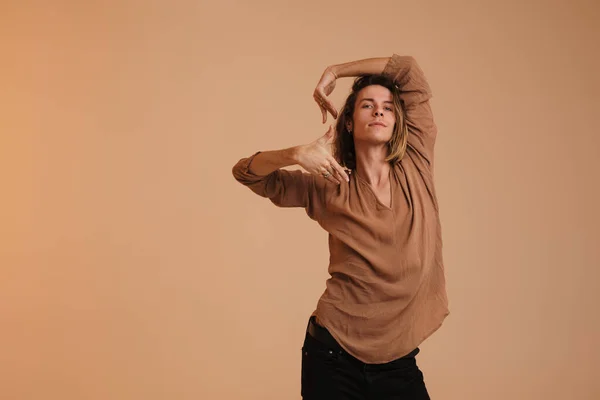 Young white man in shirt dancing and looking at camera isolated over beige wall