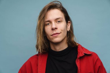 Ceketli genç bir sarışının portresi mavi arka planda kameraya bakıyor.