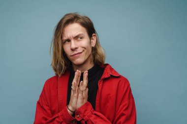 Genç beyaz adam avuçlarını bir arada tutarken yana bakıyor mavi duvarın üzerinde.