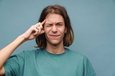 Başı çatık, başı çatık genç beyaz bir adam kafasını mavi duvarın üzerinde soyutlamış.