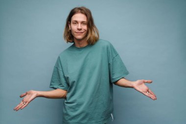 Tişört giyen, gülümseyen ve kameraya işaret eden genç beyaz adam mavi duvarın üzerinde izole edilmiş.