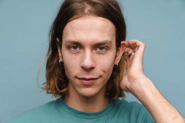 Tişörtlü gülümseyen genç sarışın bir adamın portresi mavi arka planda kameraya bakıyor.