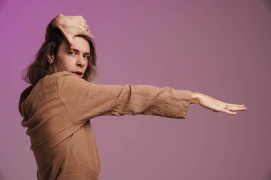 Genç beyaz adam dans ediyor ve mor duvarın üzerinden izole edilmiş kameraya bakıyor.