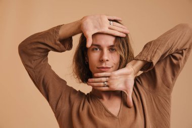 Tişörtlü genç beyaz adam dans ediyor ve bej duvarın üzerinden izole edilmiş kameraya bakıyor.