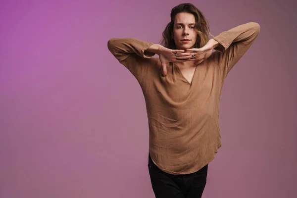 Young white man in shirt dancing and looking at camera isolated over purple wall