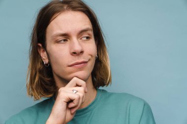 Tişörtlü gülümseyen genç sarışın bir adamın portresi. Mavi arka planda dikiliyor ve yan bakıyor.