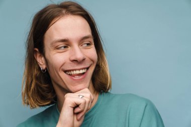 Mavi arka planda dikilmiş, gülümseyen sarışın bir adamın portresi.