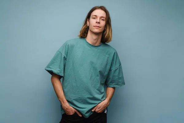 Young white man wearing t-shirt posing and looking at camera isolated over blue wall