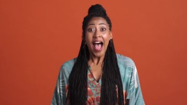 Mutlu bir Afrikalı Amerikalı kadın, stüdyoda kırmızı bir arka planda tek başına ayakta durup, kazanan jestler yapıyor.