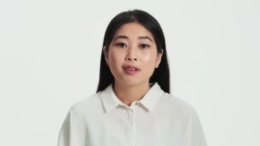 Kameraya poz veren şaşırmış Asyalı bir kadının yakın çekim görüntüsü stüdyoda beyaz arka planda izole bir şekilde duruyor.