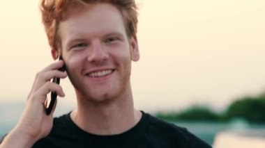 Dışarıda yürürken cep telefonunu kullanan kızıl saçlı yakışıklı bir adam.