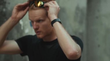 Ciddi bir sporcunun güneş gözlüğü takıp açık havada antrenman yaparken koşmasının yan görüntüsü.