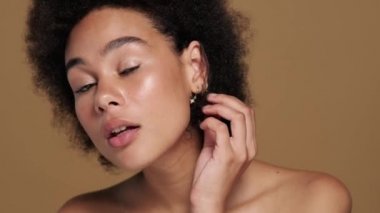 Güzel, yarı çıplak, Afro-Amerikan bir kadının, stüdyodaki bej arka planda izole bir şekilde duran aynaya baktığı yakın plan görüntüsü.