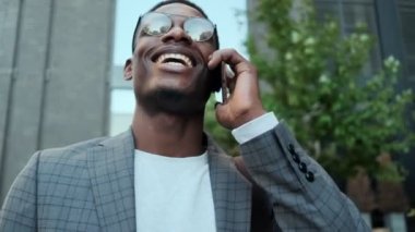 Mutlu bir Afro-Amerikan işadamı binanın önünde dikilirken cep telefonuyla konuşuyor.