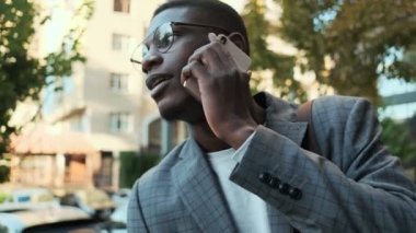Yakışıklı bir afro-amerikan işadamı binanın dışında beklerken cep telefonuyla konuşuyor.