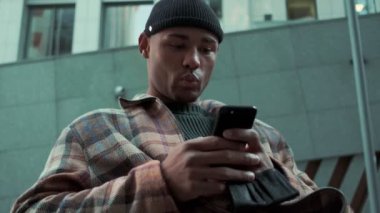 Yakışıklı bir Afro-Amerikan adam cep telefonunu sokakta kullanıyor.