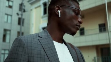 Sokakta yürürken telefonuyla kulaklık takan, gülümseyen Afro-Amerikan bir iş adamının yakın görüntüsü.